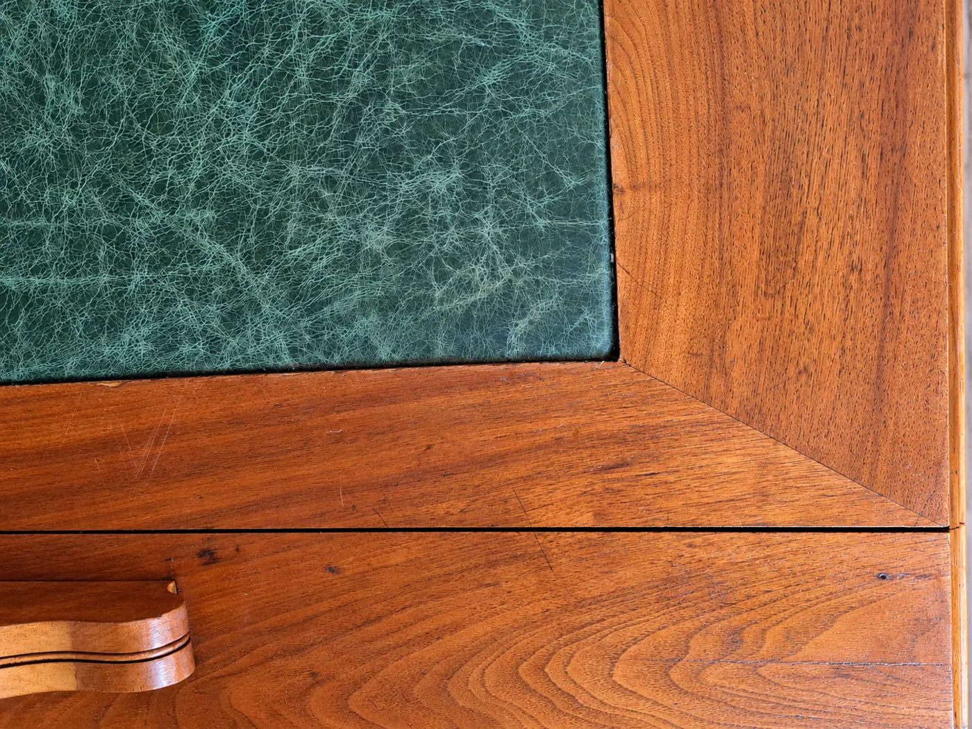 Ecke einer Tischplatte mit grüner Lederauflage und Holzrahmen